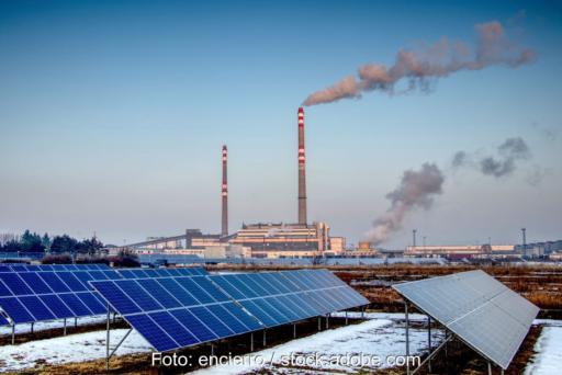 Solarpark in der Umgebung einer Industrieanlage mit rauchenden Schloten.