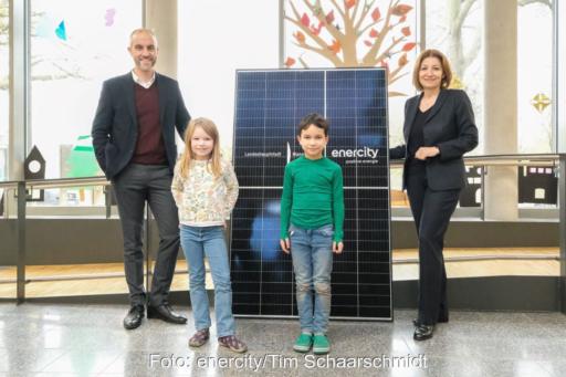 Zwei Kinder udn zwei Erwachsene vor einer Solaranlage in einer Schulaaula.