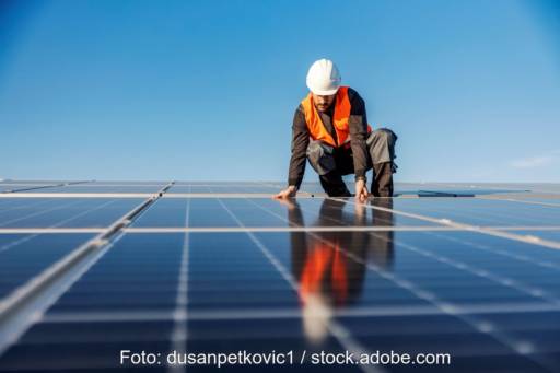Arbeiter mit Schutzhelm und Weste montiert auf einem Flachdach Solarmodule
