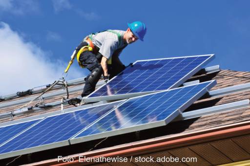 Handwerker verlegt Photovoltaik-Module auf einem Walmdach