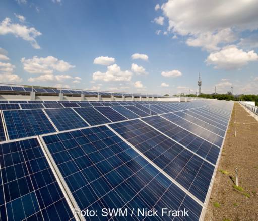 Blick über eine ÜPV-Anlage auf dem Dach mit dem Münchener Fernsehtrum am Horizont.