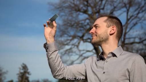 Ein Mann hält eine Solarzelle in die Höhe - semitransparente organische Photovoltaik in der Forschung.