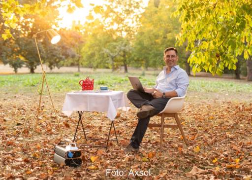 Mann an Tisch im Garten mit Laptop, roter Teekanne und mobilem Stromspeicher - Symbolbild für Axsol-Übernahme durch Loh.