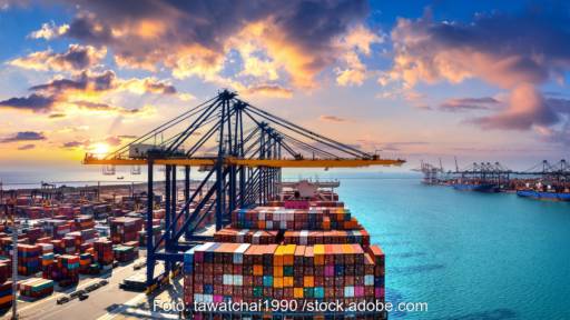 Kräne und Containerschiffe im Hafen bei leuchtend rosa Wolken - Symbol für Seefracht