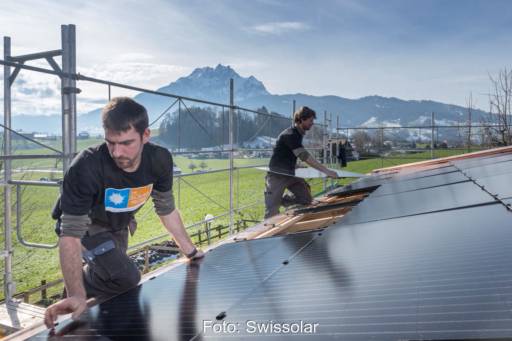 2 Installateure montieren Solarmodule - im Hintergrund schneebedeckte Berge.