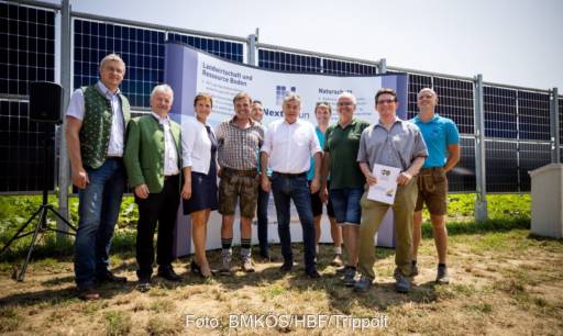 Frauen und Männer bei der Einweihung vor vertikal aufgebauten Solarmodulen.