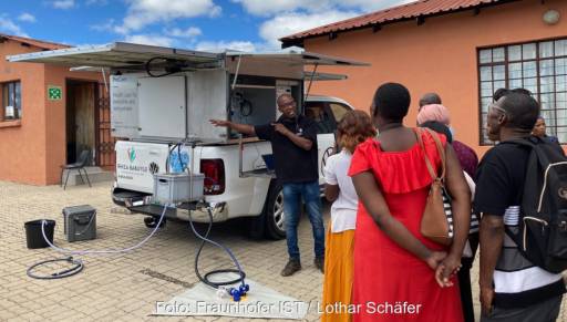 Im Bild ist die mobile medizinische Versorgungsplattform mit ausgeklappten PV-Modulen zu sehen. Der Fahrer und Operator des Systems erläutert Umstehenden den Aufbau.