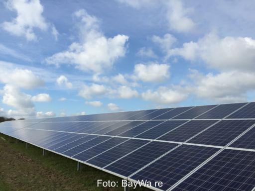 Freiflächensolaranlage auf grüner Wiese unter blauem Himmel mit Wolken.