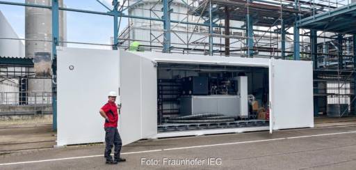 Mann mit Helm hält Tür zu einem Container mit Großwärmepumpe auf.