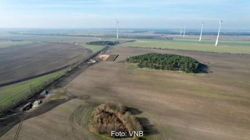 Blick über flaches Land auf einige Windenergie-Anlagen mit hohem Turm und kleinem Rotor.