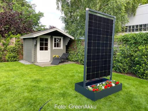 Ein hochkant stehendes Solarmodul mit Blumenkasten vor einem Gartenhäuschen.