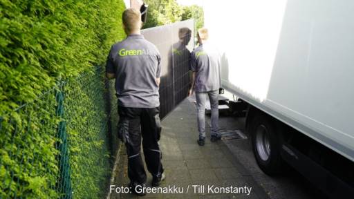 Im Bild zwei Männer, die ein unverpacktes PV-Modul tragen, Greenakku bietet eine verpackungsfreie Direktlieferung von Solarmodulen an.