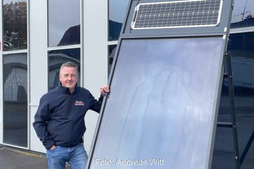 Im Vordergrund ein Luftkollektor. Daneben stehend Jörg Haustein. Im Hintergrund eine Fassade mit Luftkollektoren.