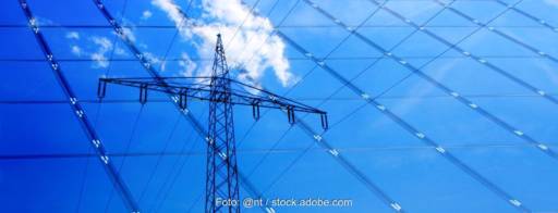 Ein Strommast, blauer Himmel und Wolken spiegeln sich in einer Solarfassade.