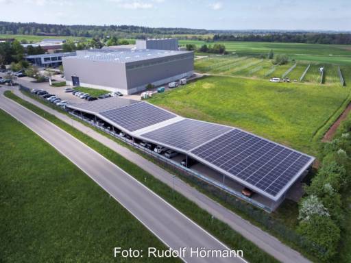 Luftbild mit wellenförmigen PV-Parkplatzdach neben Firmenzentrale