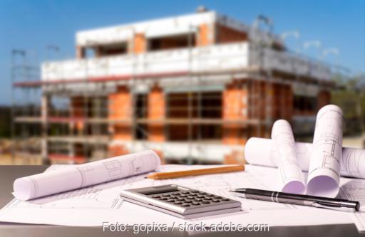 Baupläne und Taschenrechner im Vordergrund - hinten ein Neubau