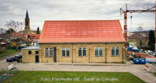 Im Bild eine historische Turnhalle, die mit einer ziegelroten Photovoltaik-Anlage mit MorphoColor-Beschichtung der Solargläser versehen ist.
