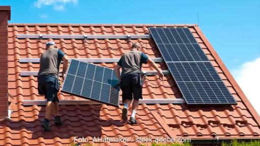 Im Bild zwei Männer, die ein Photovoltaik-Modul auf ein Dach schleppen, die Initiative SolAixQ ⎼ Solar lernen im Aachener Quartier bildet Solarhelfer:innen aus.