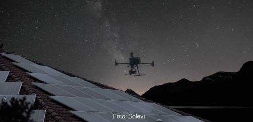 Drohne schwebt über Dach-PV-Anlage vor Sternenhimmel - Messung mit Elektrolumineszenz-Verfahren.