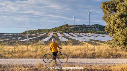 Mensch mit Fahhrad steht auf einem Weg und schaut zu Solarpark und Windenergie-Anlagen. Symbolbild für Photovoltaik und Windenergie in der Region Kastilien und Leon, Spanien.