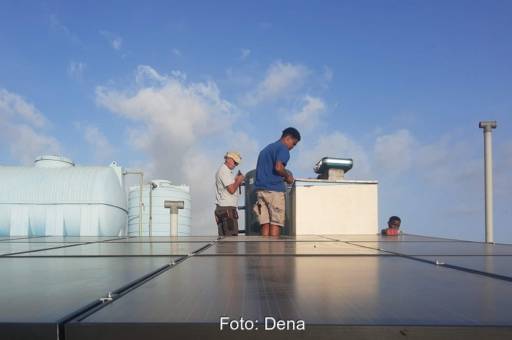 Mehrere Personen hinter einer Solardachanlage sowie Produktionstürmen im Hintergrund.