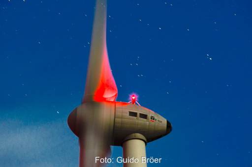 Nachtaufnahme (Langzeitbelichtung) der Gondel einer Enercon-Windenergieanlage Typ E-101 Mit roter Nachtbeleuchtung vor Sternenhimmel.