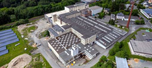 Luftaufnahme mit einem sanierungsbedürftiges Gewerbeareal mit Photovoltaik in der Nachbarschaft.