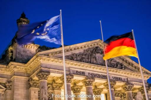 Beleuchtetes Gebäude des Deutschen Bundestages mit Europa- und Deutschlandflagge im Vordergrund.