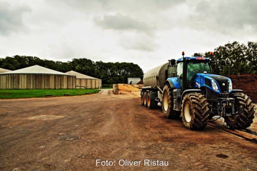 Landwirtschaftlicher Hof mit Biogasfermentern im Hintergrund und einem Traktor im Vordergrund.
