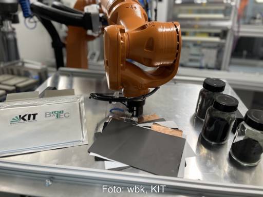Bild zeigt einen Roboterarm, einige Folien und schwarzes Granulat in Gläsern - Batterie-Recycling am KIT.