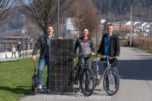 Drei Personen mit Fahrrädern auf einem Radweg mit einem großen Solarmodul