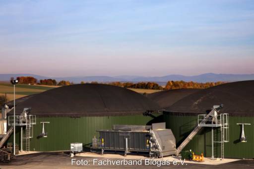 Biogasfermenter vor Gebirgskette am Horizont bei Sonnenuntergang.