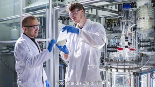 Im Bild zwei Männer im Labor mit einer Flasche des Energiespeichermaterials Preußisch Weiß für Natrium-Ionen-Batterien.