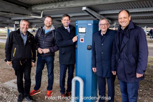 Fünf Männer mit dunklen Anzügen neben blauer Ladesäule - Ladepunkte für E-Autos in Norddeich