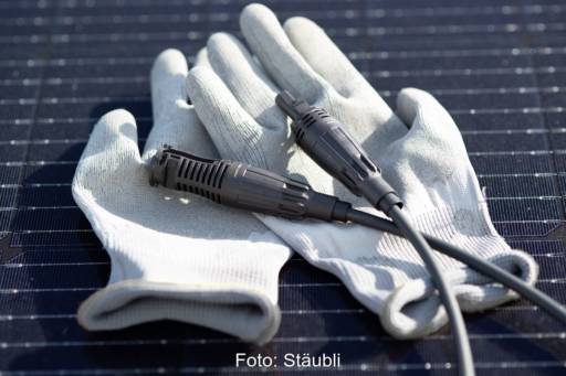 Ein paar Handschuhe und zwei Teile eines Steckverbinders auf einem Photovoltaik-Modul