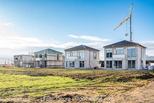 Neubaugebiet: Häuser im Rohbau mit Kran, im Vordergrund Acker.