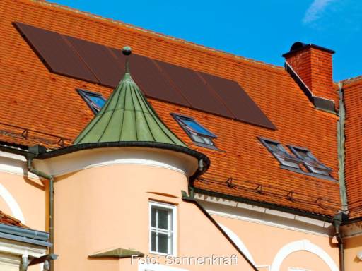 Ein denkmalgeschütztes Gebäude mit Türmchen und einem Ziegelschrägdach mit integriertem rotem Solarmodul.