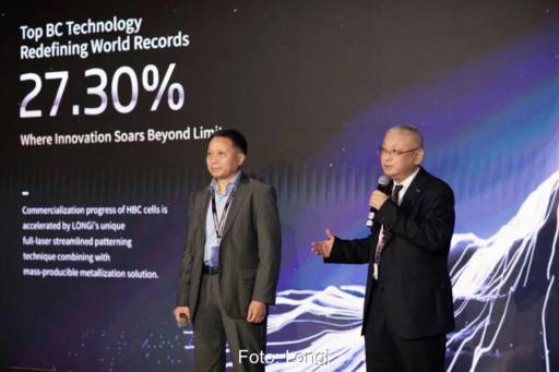 Zwei Personen auf einer Bühne vor einer Präsentation zu Solarzellen-Effizienz wenden sich an das Publikum.