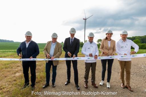 Sechs Menschen durchschneiden Band auf Feldweg, dahinter Windenergie-Anlage.