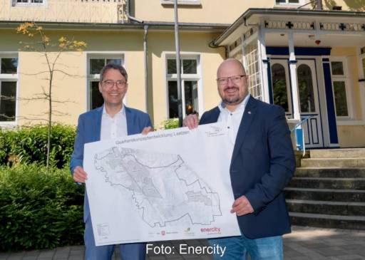 Zwei Männer stehen vor Haus und halten Plan von Laatzen hoch - Startschuss für die Wärmeplanung.