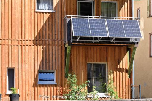 Eine Hausfassade mit Holzverkleidung, daran ein Balkon mit einer Steckersolaranlage mit 2 Photovoltaik-Modulen