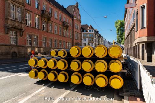 Stapel von Rohren zum Wärmetransport auf einer Straße in einer Stadt mit historischen Gebäuden.