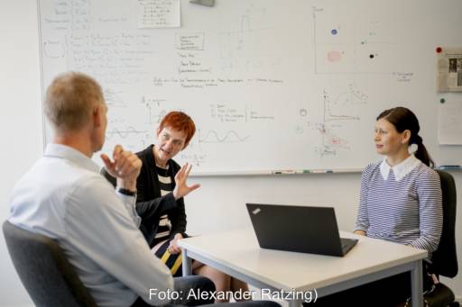 Ein Mann und eine Frau gestikulierend im Gespräch, eine junge Frau sitzt hinter einem Computer - Forschungsgruppe für Energiewende-Kommunikation.