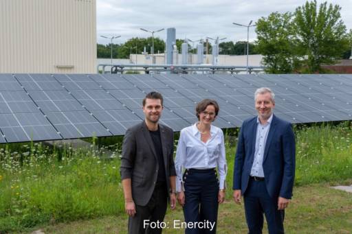 Drei freundlich blickende Personen vor einer PV-Anlage und einer Industrieinstallation.