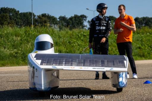 Zwei Menschen stehen hinter einem Solarauto, ein schmaler flacher Flitzer mit einem seitlichen Flügel mit Solarzellen.
