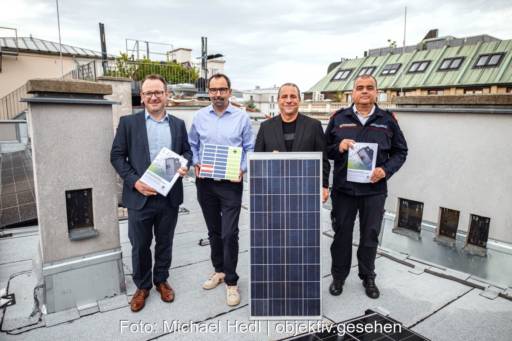Vier Herren präsentieren auf einem Dach neben einem PV-Modul Broschüren, die einen Leitfaden zum Brandschutz enthalten.