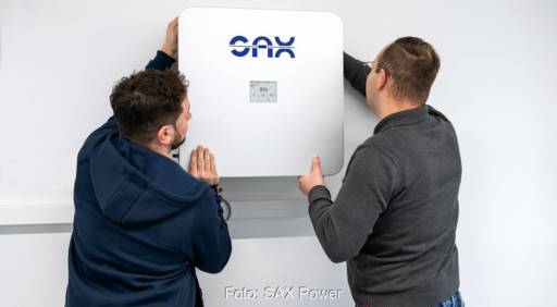 Zwei Männer hängen einen Der SAX Power PV-Speicher an die Wand.
