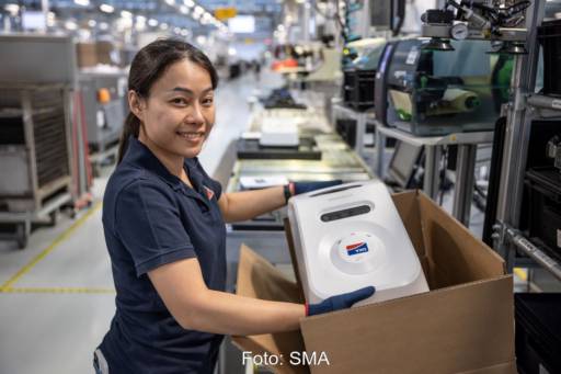 Eine Frau in einer Fabrik präsentiert eine Box mit einem Ladegerät.