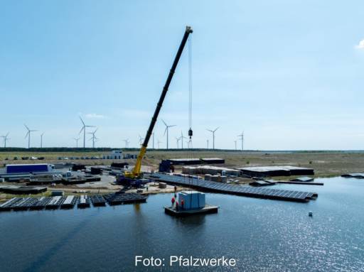 Verladung eines Trafos auf eine schwimmende Plattform in einem See per Kran von Land.