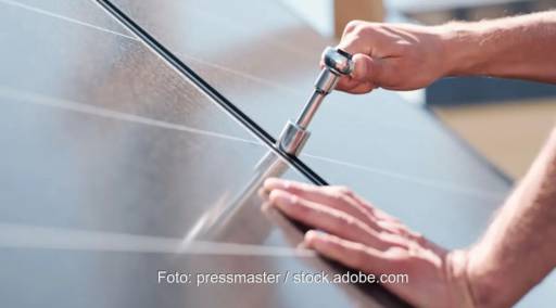 Im Bild eine Hand mit einer Ratsche, die ein Photovoltaik-Modul befestigt. Die EnWG-Novelle soll Hürden für Solarinstallationsunternehmen abbauen.